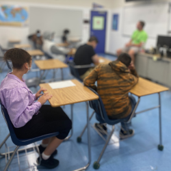 Students in classroom with teacher sitting on desk